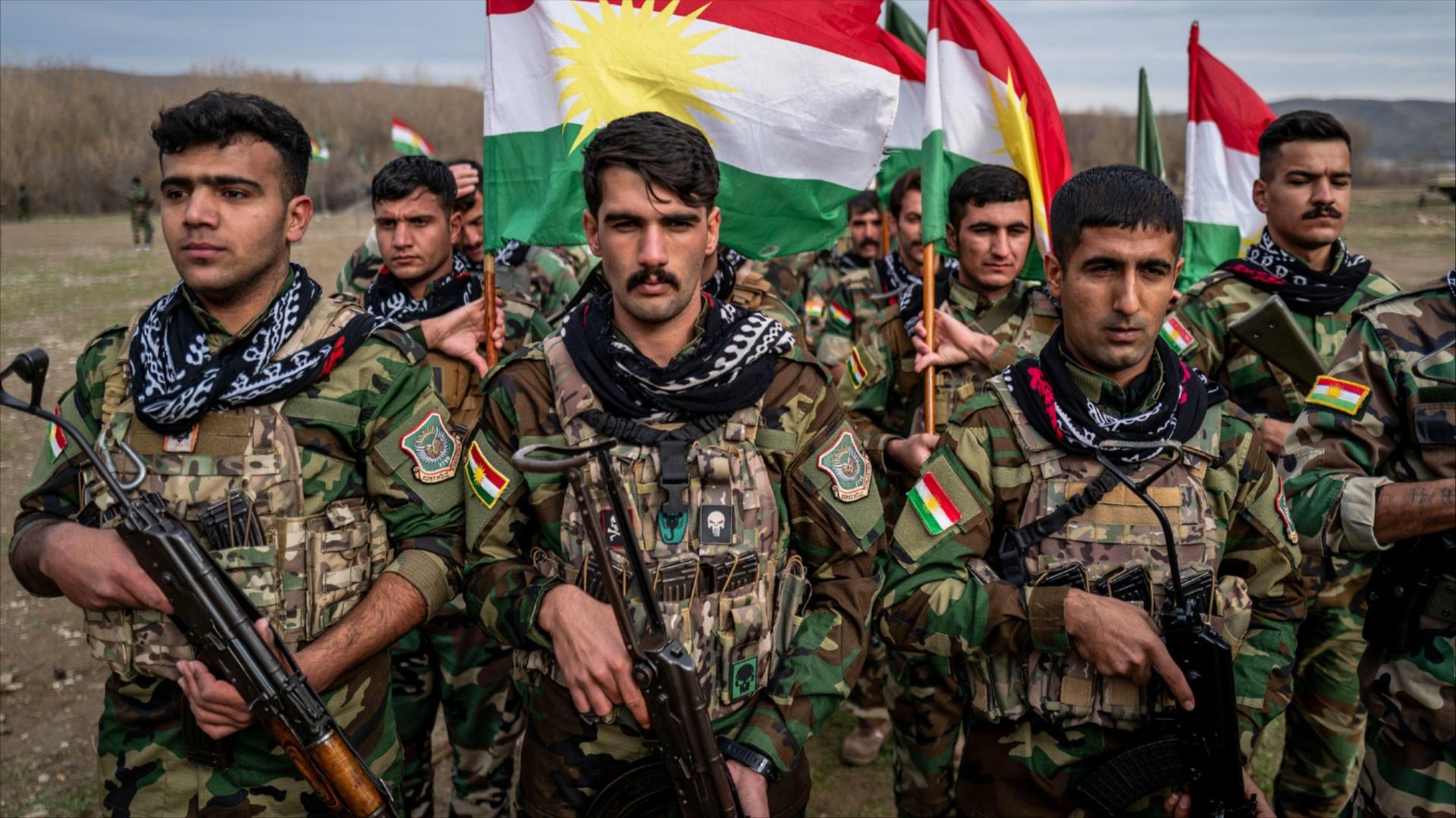 People in military uniforms holding guns and Kurdish flags