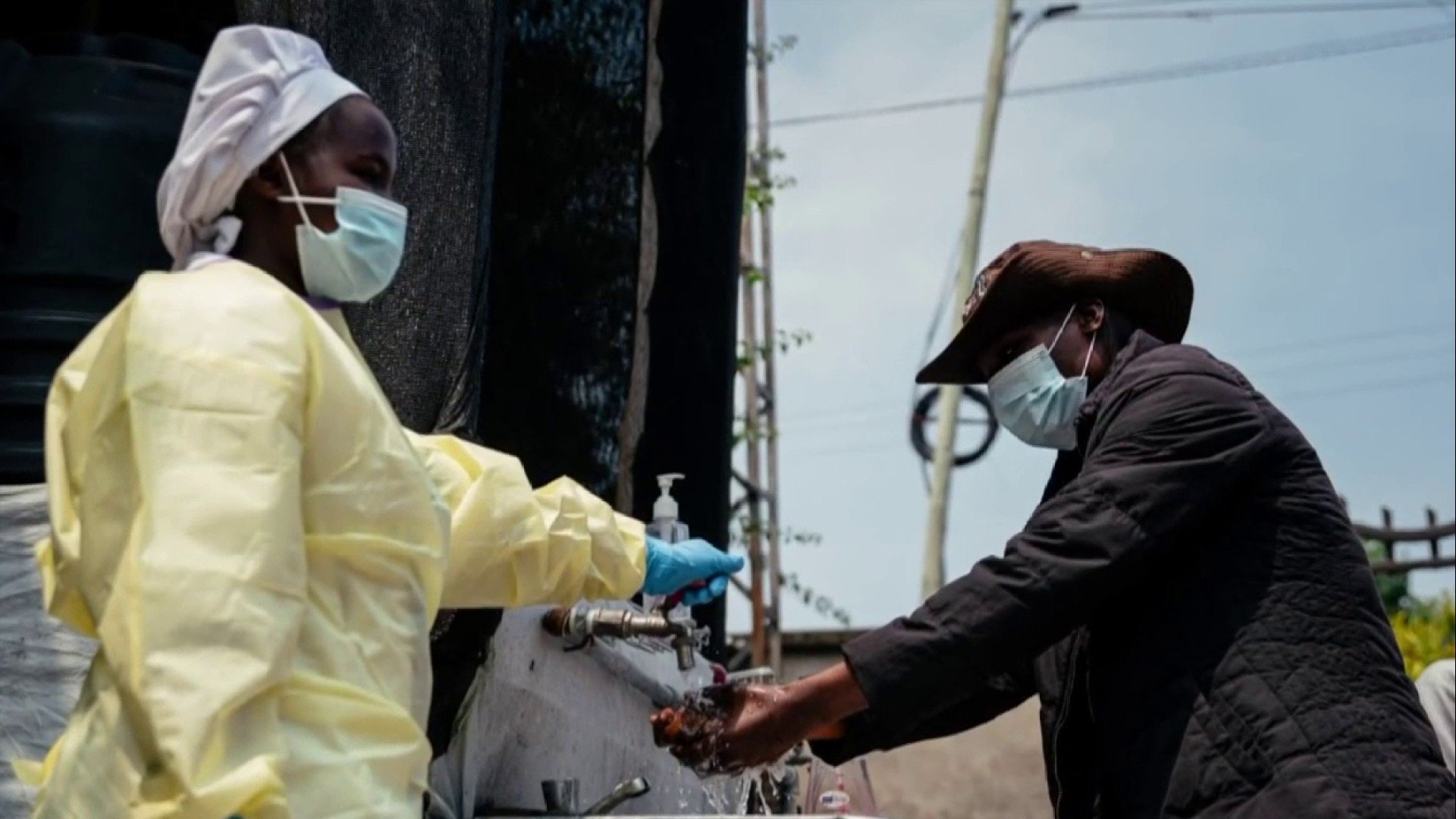 Person in protective clothing helping another person wash their hands