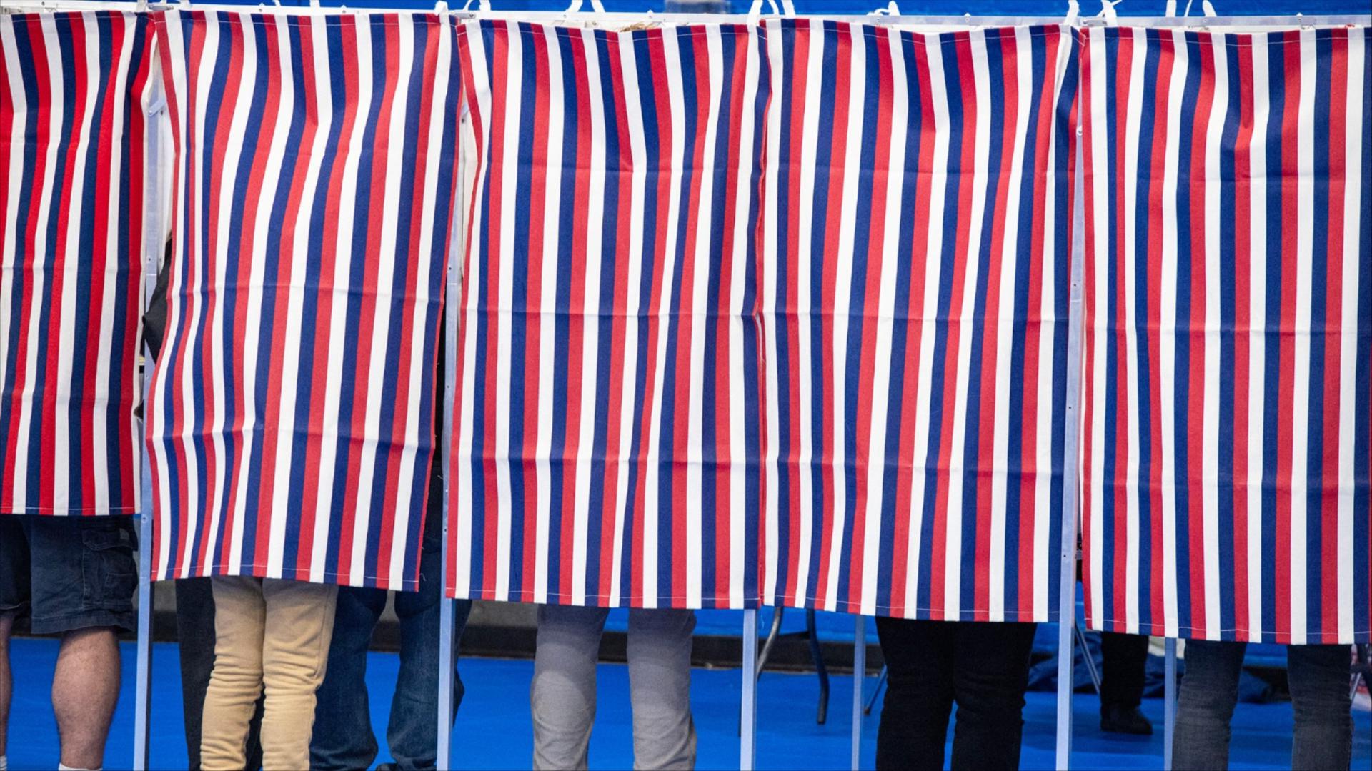 Legs are seen below red, white and blue voting booth curtains