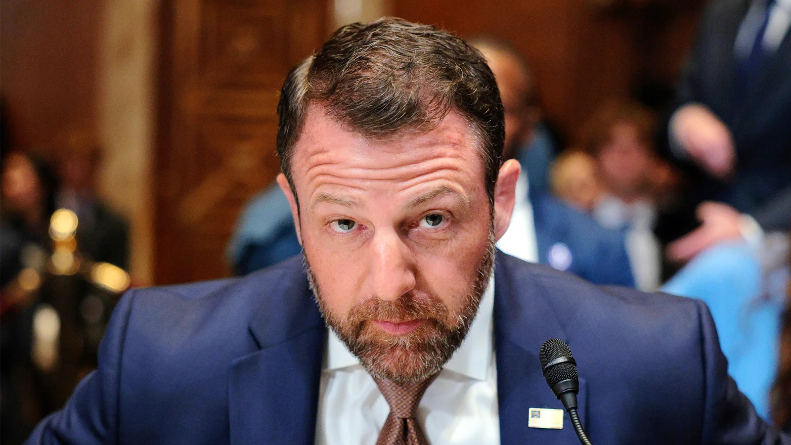 Markwayne Mullin looks up at the camera as he is about to sit down.