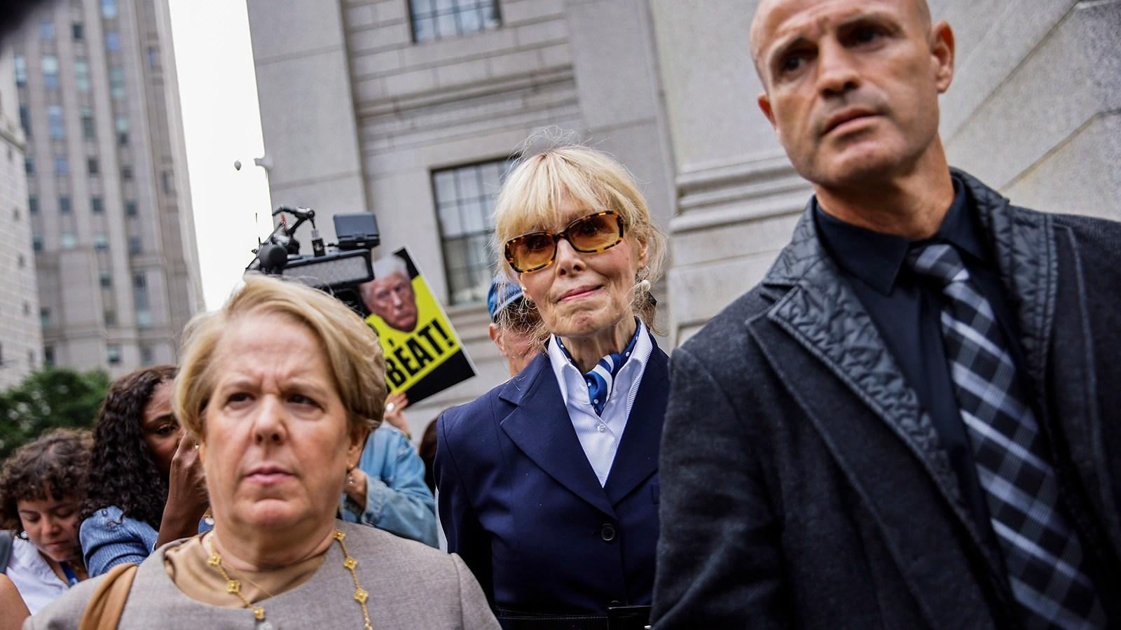 Jean Carroll walks behind a man, right, and a woman.