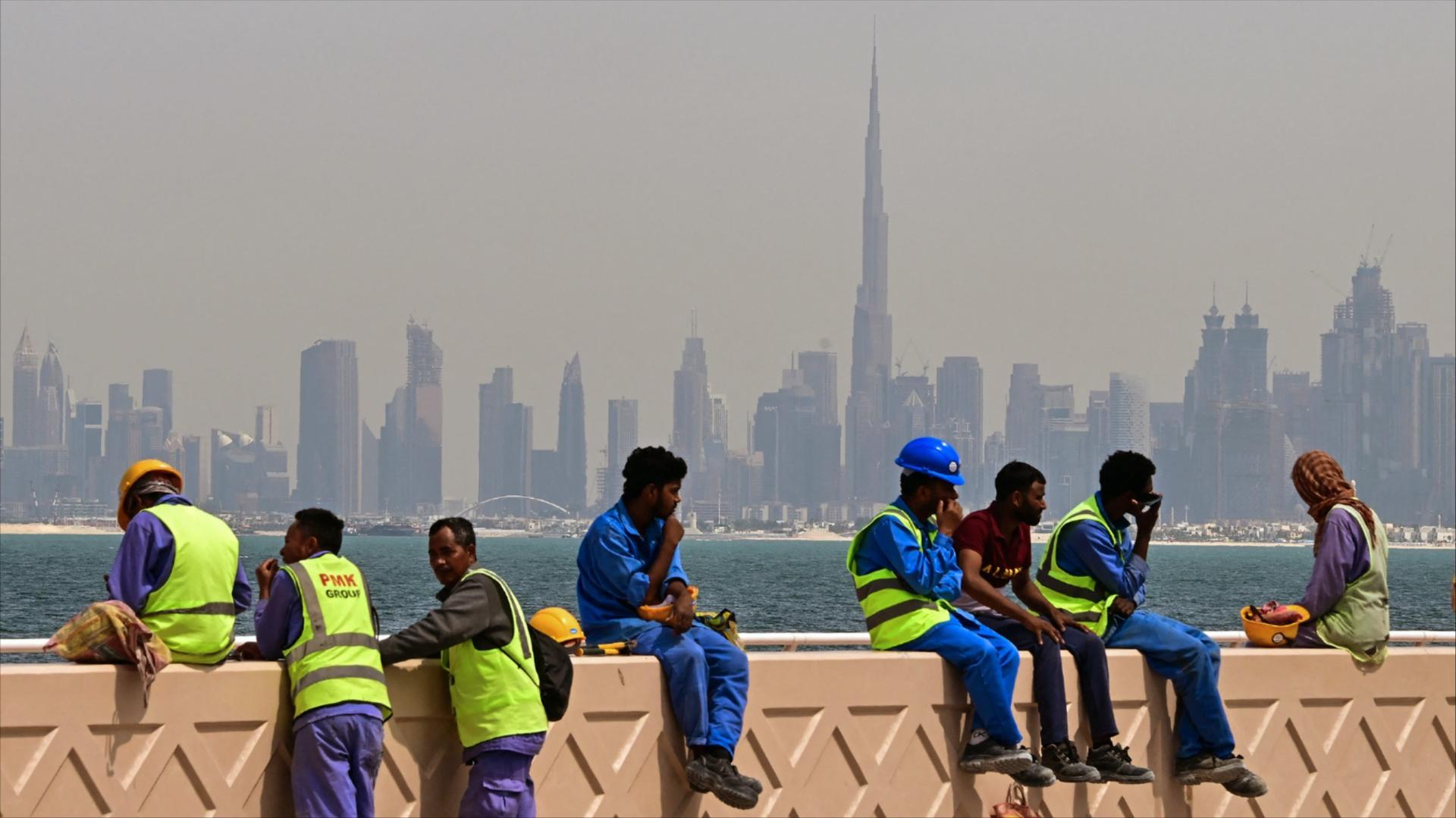 Workers sit on a wall against the Dubai backdrop