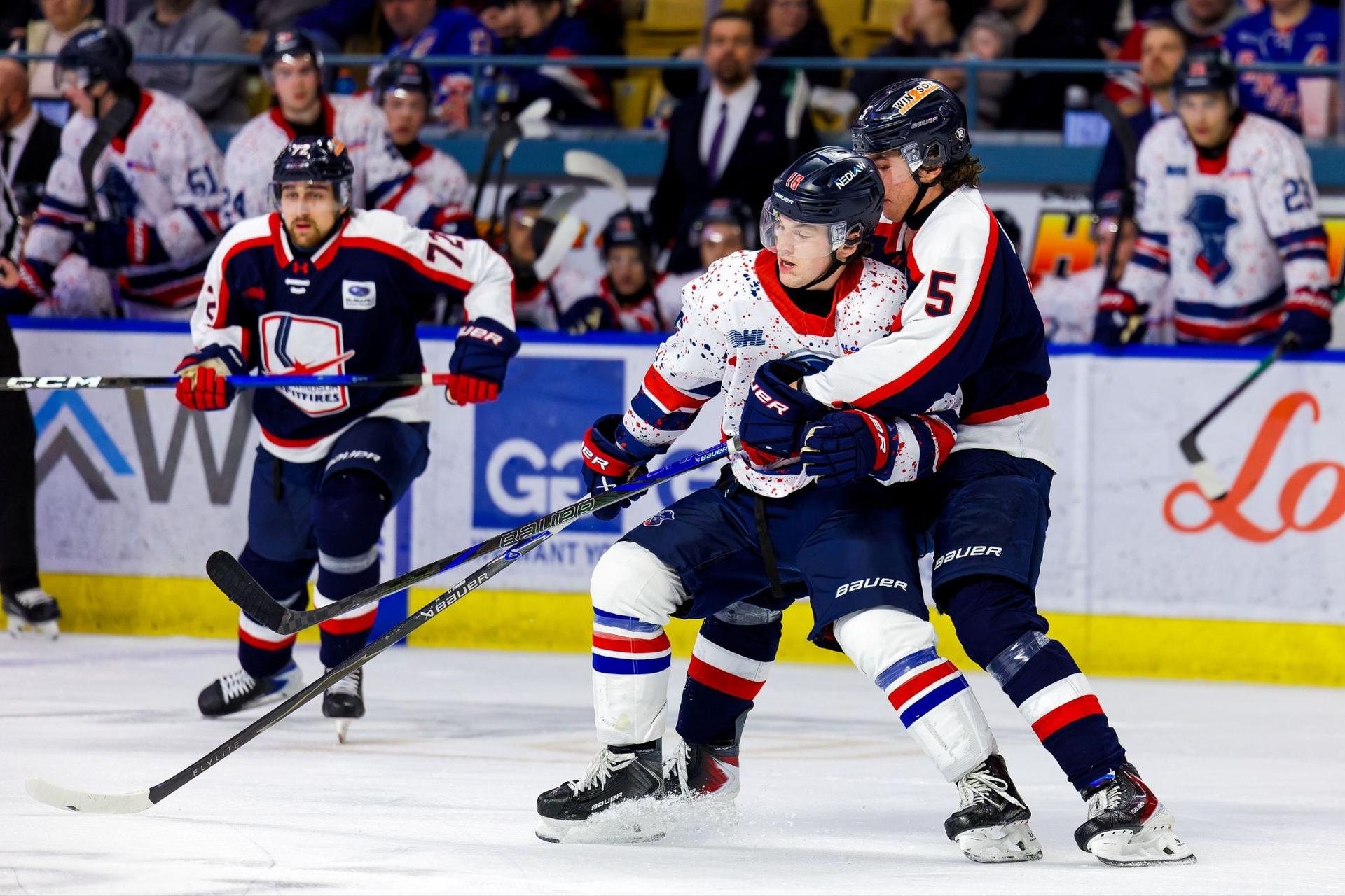 Three hockey players skate on the ice as the rest of the team looks on.
