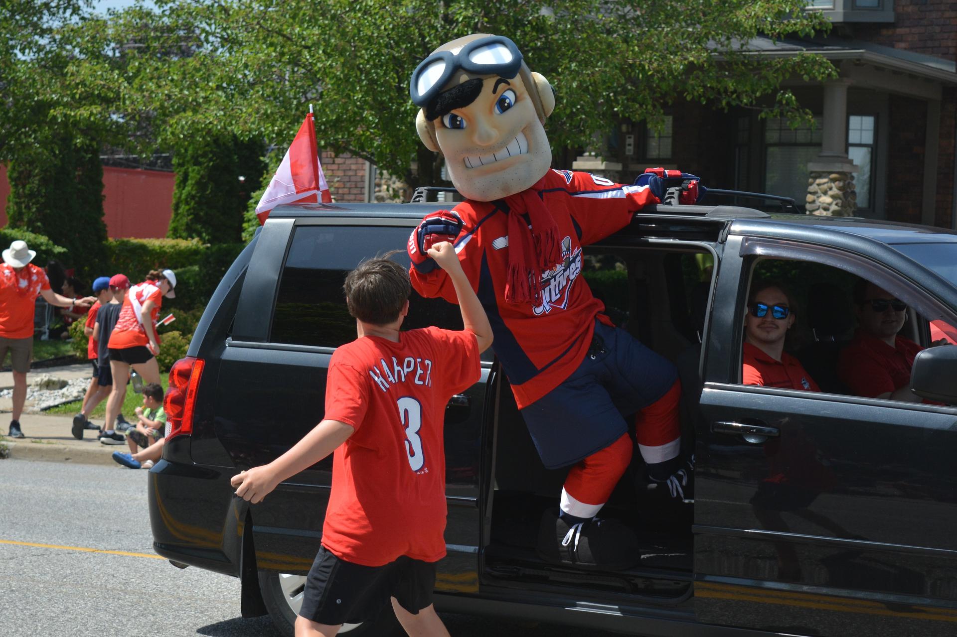 Windsor Spitfires mascot Bomber exchanges a fist bump with an excitable kid during the Canada Day Parade on Ouellette Avenue..