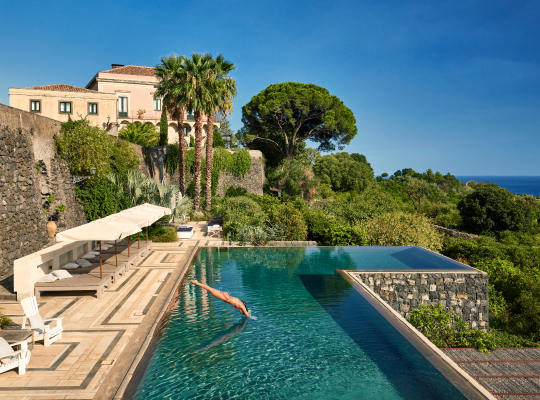 A person diving into a pool overlooking the sea.
