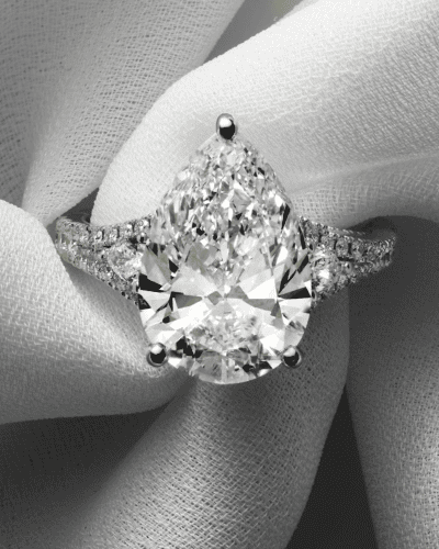 A pear shaped diamond engagement ring on a soft white fabric background.