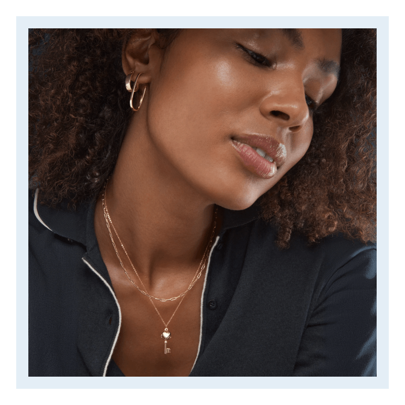 Close-up of a woman wearing fine yellow gold jewelry, including hoop earrings and layered necklaces.