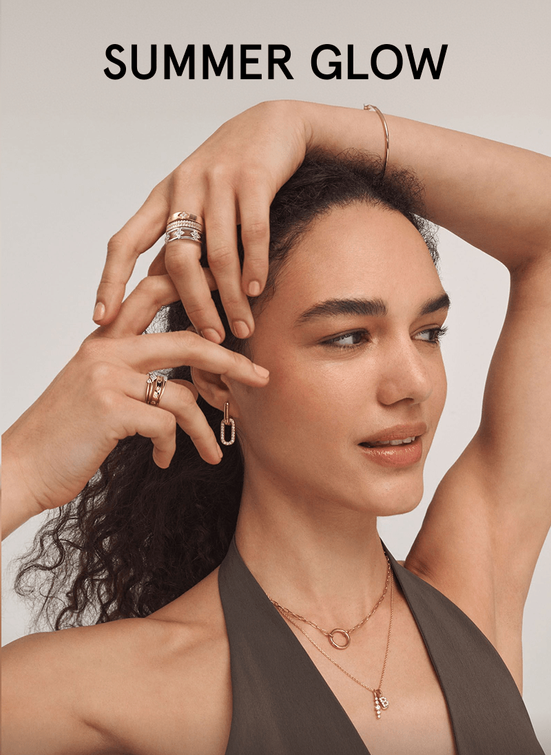 Woman wearing layered necklaces, stacked rings, hoop earrings and a bangle bracelet.