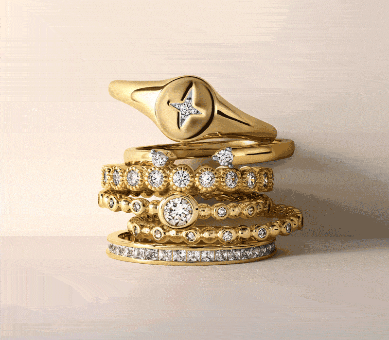 Various yellow gold rings with diamond details stacked one on top of the other. Yellow gold diamond hoop earrings.