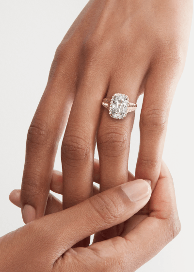 Close-up of a hand wearing an oval-cut diamond engagement ring with a diamond-accented gold band.