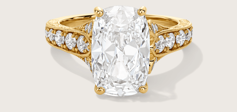Yellow gold cushion-cut engagement ring, with four-prong setting and diamonds along the band.