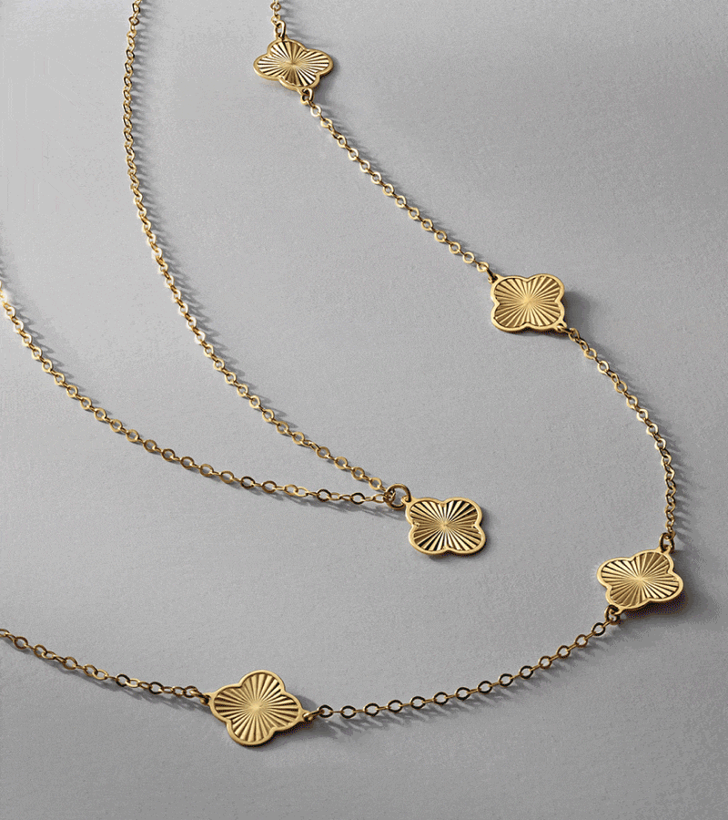 Yellow gold necklace with four-leaf clover accents. Stack of gold rings featuring colorful oval gemstones.