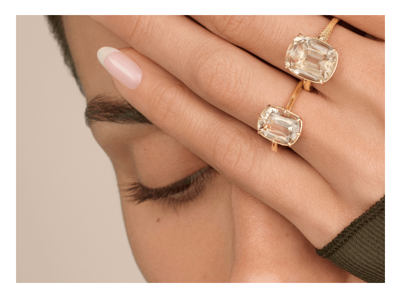 Close-up of two gold rings featuring large cushion-cut clear gemstones and diamond-accented bands.