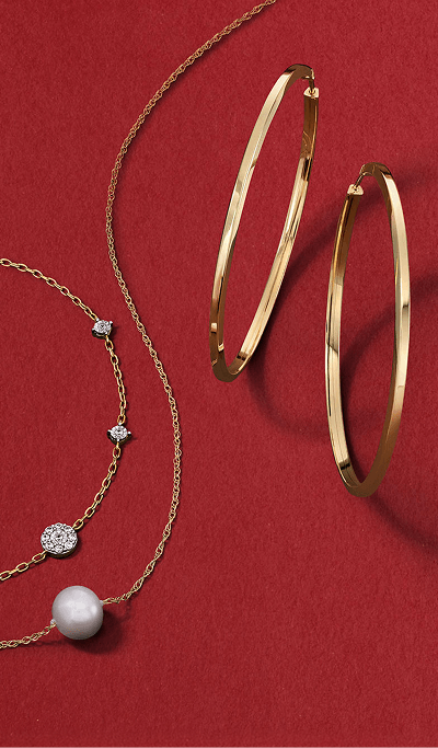 Yellow gold hoop earrings displayed with delicate gold necklaces featuring diamond and pearl accents.