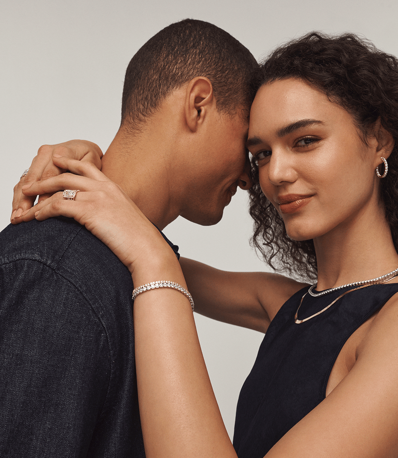 A model hugging another, wearing a rectangular diamond ring with matching diamond and gold jewellery.