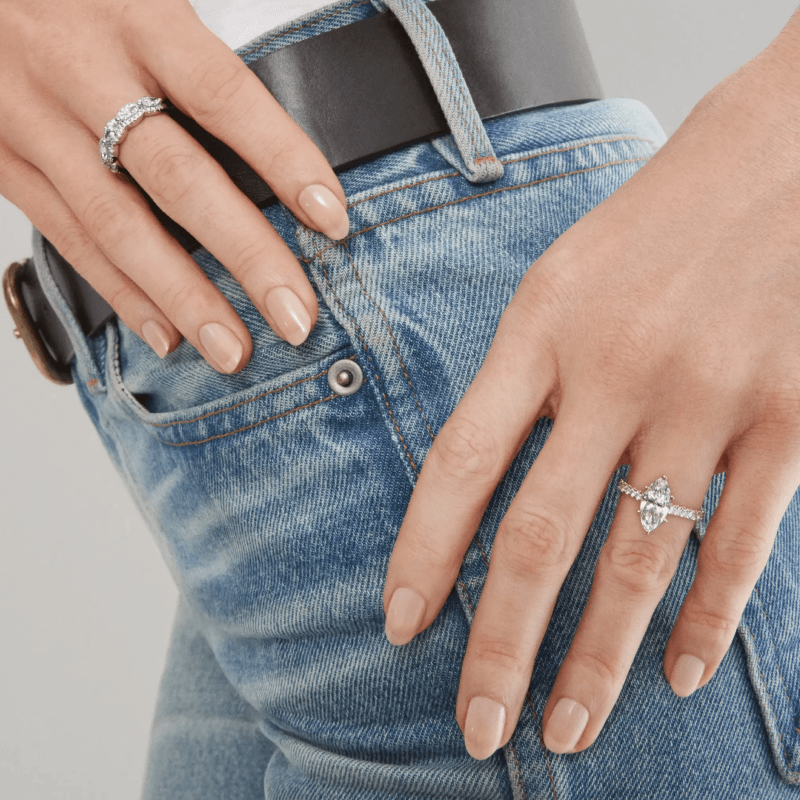 A model wearing a marquise diamond engagement ring and diamond band with casual denim styling.