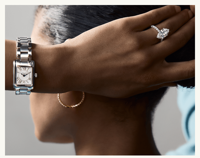 Model wearing diamond shaped ring, silver watch & gold set diamond hoops.