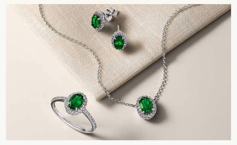Set of diamond jewelry including studs, pendant chain & ring with emerald green gemstones.