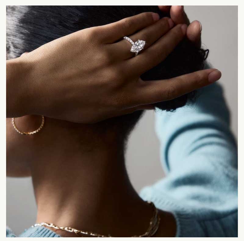 Model with large marquise cut diamond ring, gold hoops & chain necklace.