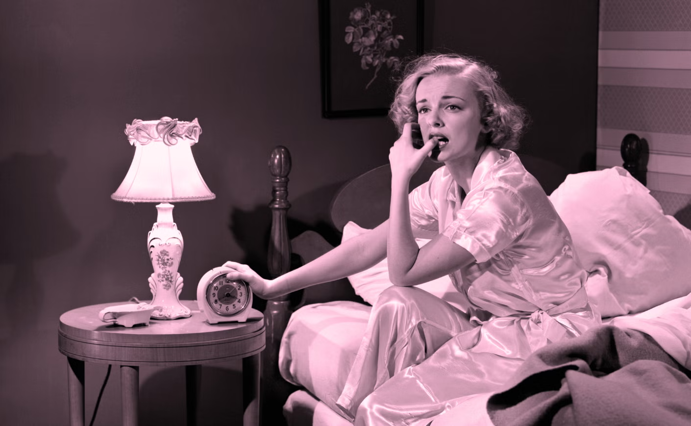 A 1950s era woman nervously chewing on her thumb while sitting up in bed