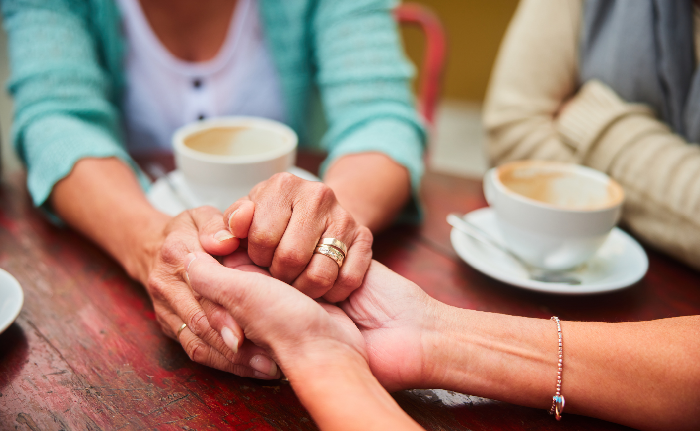 Women holding hands over a table with coffee cups