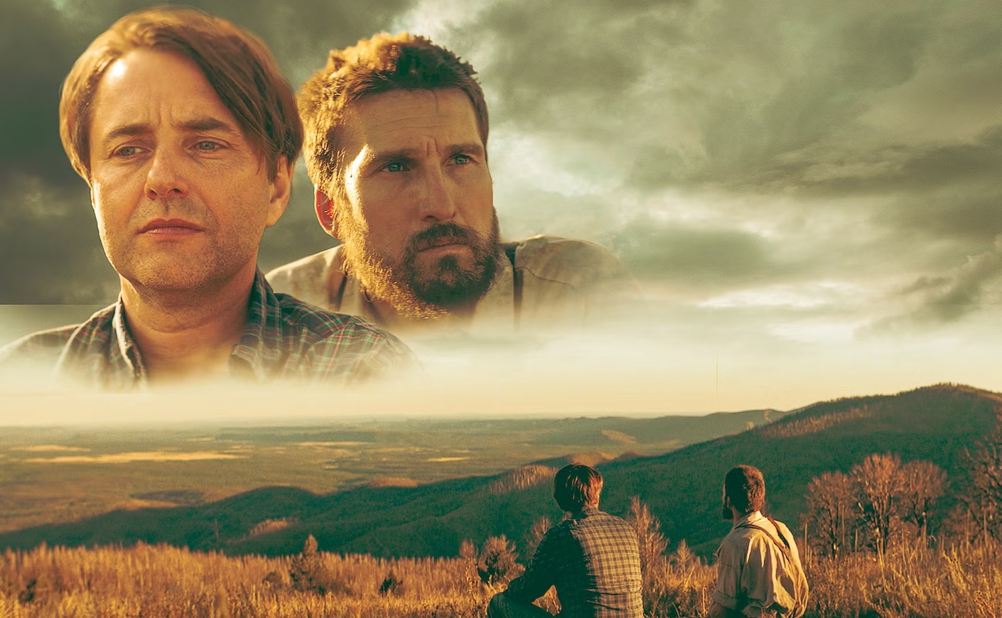 Two men looking out over a vast prairie like landscape with hills in the background