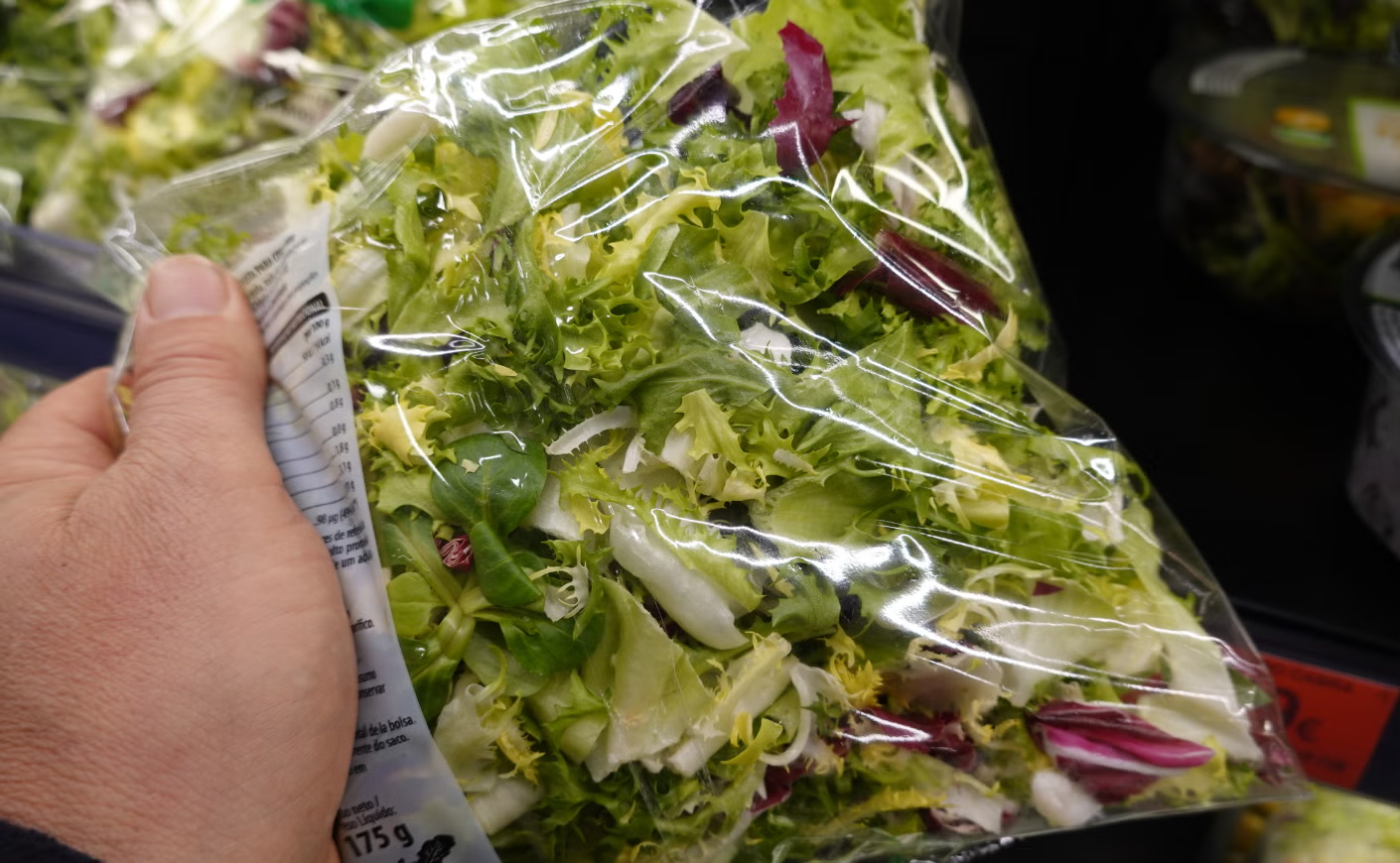 A hand picking up bagged lettuce in the grocery store
