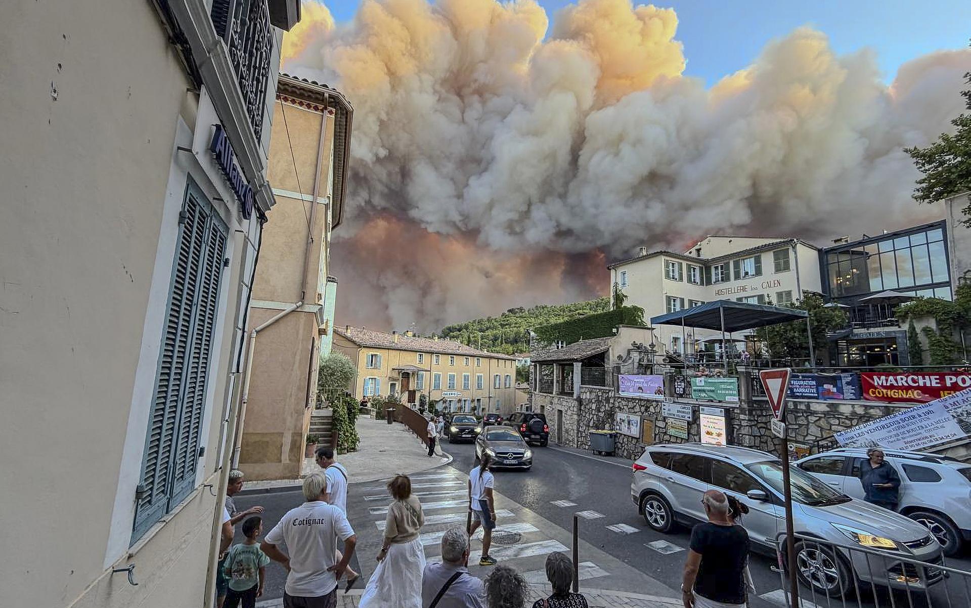 Bystanders stop in the street as a plume of smoke and flames towers over a French town