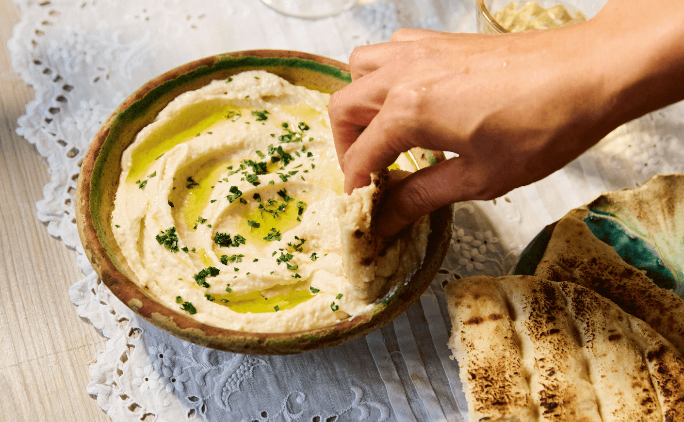 A hand dipping pita into a bowl of Greek garlic dip.