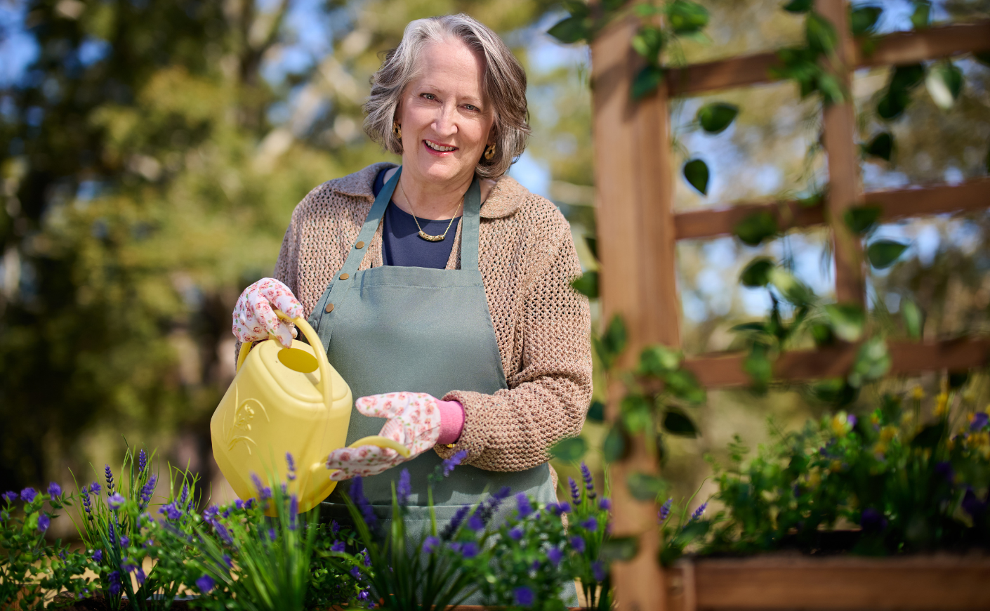 A mature white woman standing in her garden and watering it with a yellow watering can