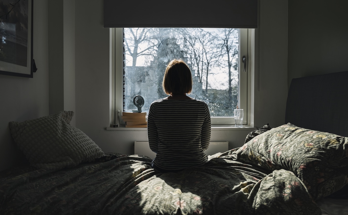 Woman sitting on her bed in front of an open window