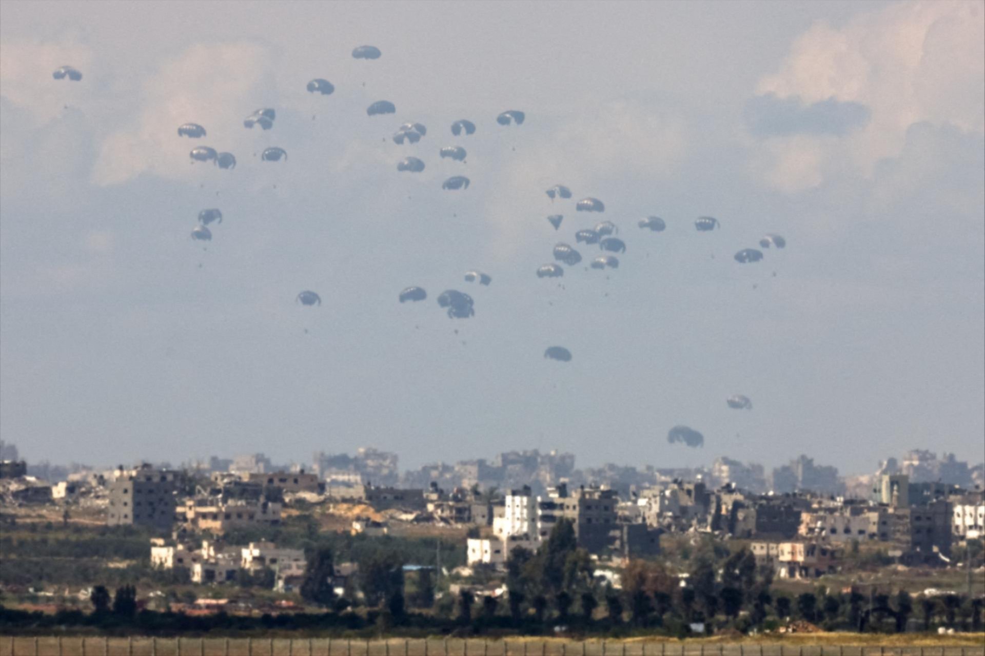 Humanitarian aid falls through the sky towards the Gaza Strip, as seen from Israel