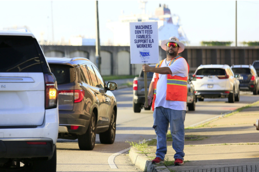 A striking port worker holding signs stands at the entrance to the Port of New Orleans, Louisiana, the United States, on Oct. 2, 2024. About 45,000 dock workers walked out at 36 U.S. ports amid fears of job loss in an AI-driven future. Lan Wei/Xinhua/Getty Images