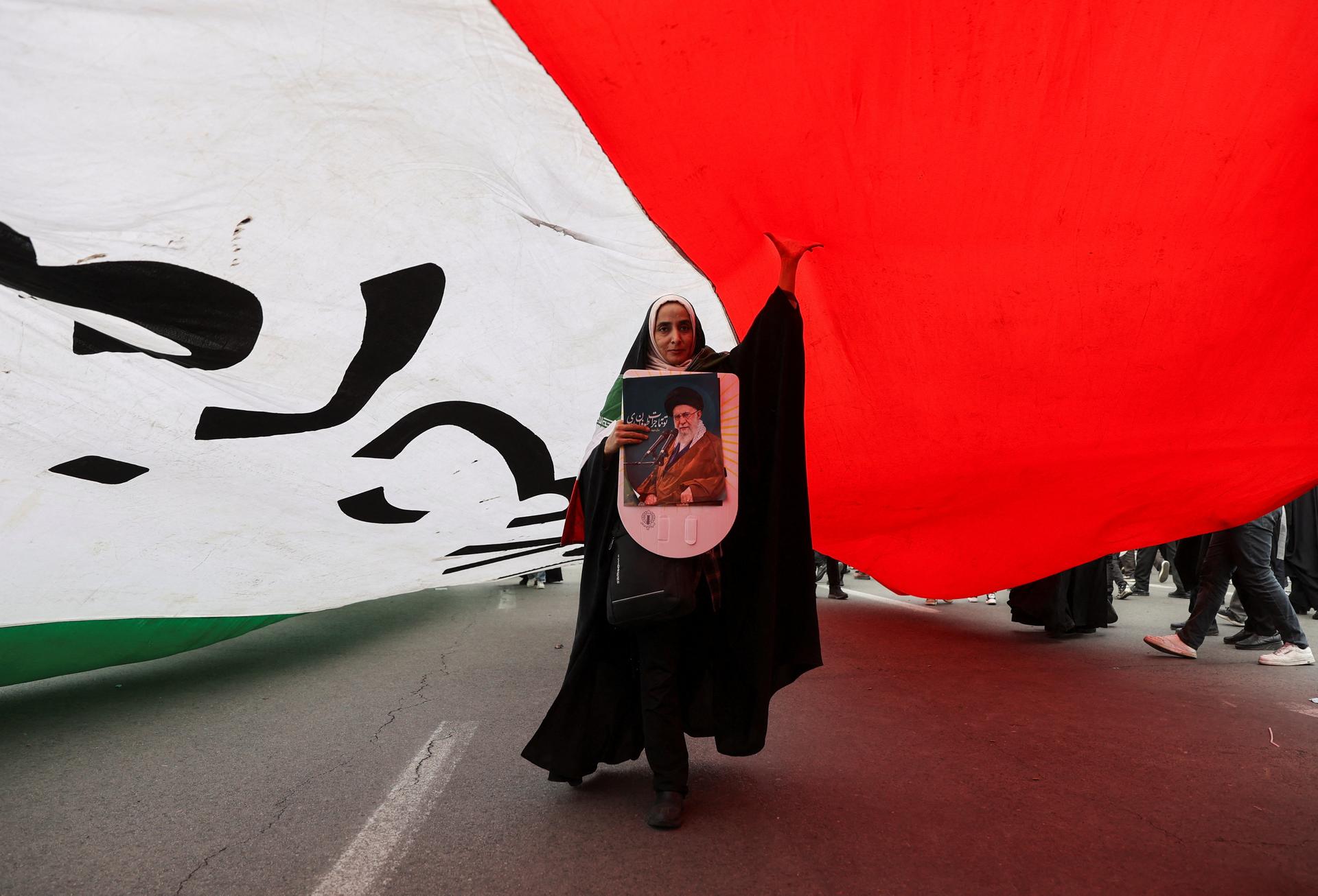 An Iranian woman holding a poster depicting Iran’s Supreme Leader Ayatollah Ali Khamenei walks under a large flag during the forty-seventh anniversary of the Islamic Revolution in Tehran, Iran, on February 11, 2026.