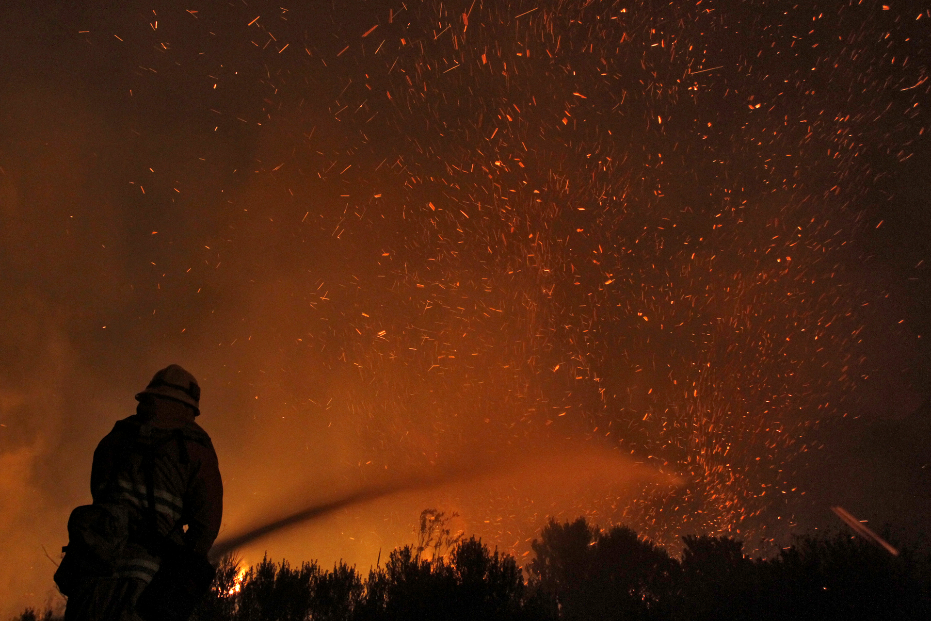 The silhouette of a firefighter shooting a hose at a wildfire