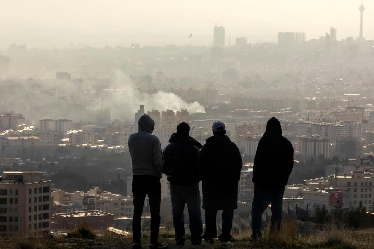 Men watch from a hillside as a plume of smoke rises after an explosion on March 2, 2026 in Tehran, Iran. 