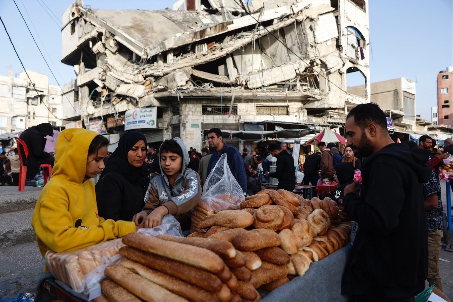 Palestinians sell bread on a street beneath a destroyed building in Gaza City’s Zawiya market on February 18, 2026, on the first days of the holy fasting month of Ramadan. 