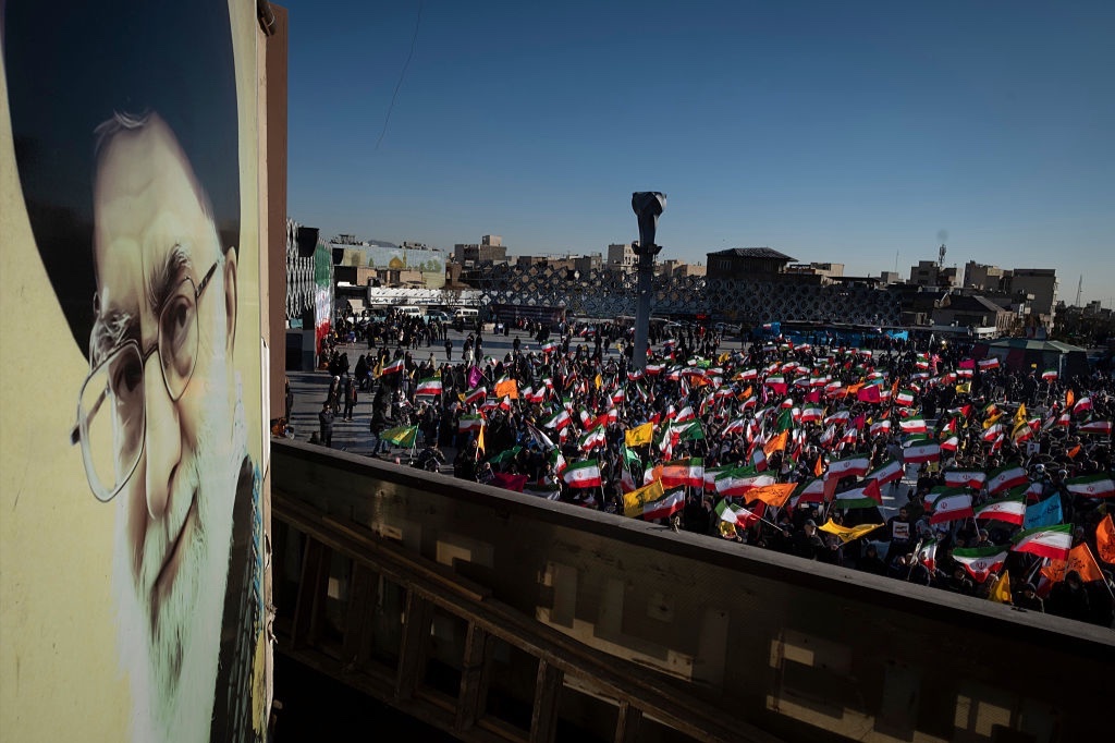 Iranian people hold the national flags next to a portrait of Iran's Supreme Leader, Ayatollah Ali Khamenei, during a pro-government rally in opposition to the recent protests in Iran in southern Tehran on December 30, 2025.