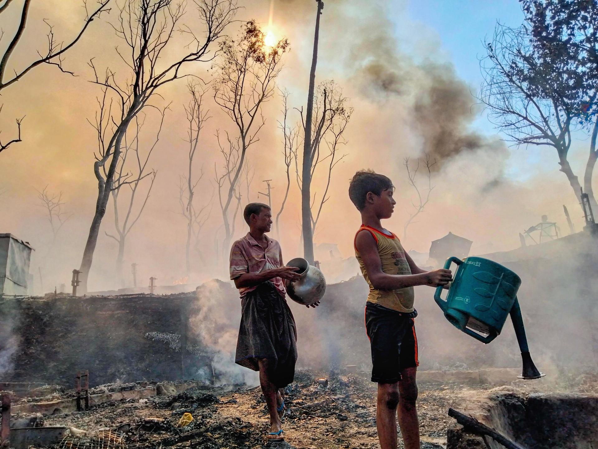 A father and son, working to reclaim what remains of a home reduced to ash, douse smoldering earth with water after a fire tore through their section of the encampment, in Cox's Bazar, Bangladesh, on December 24, 2024. 