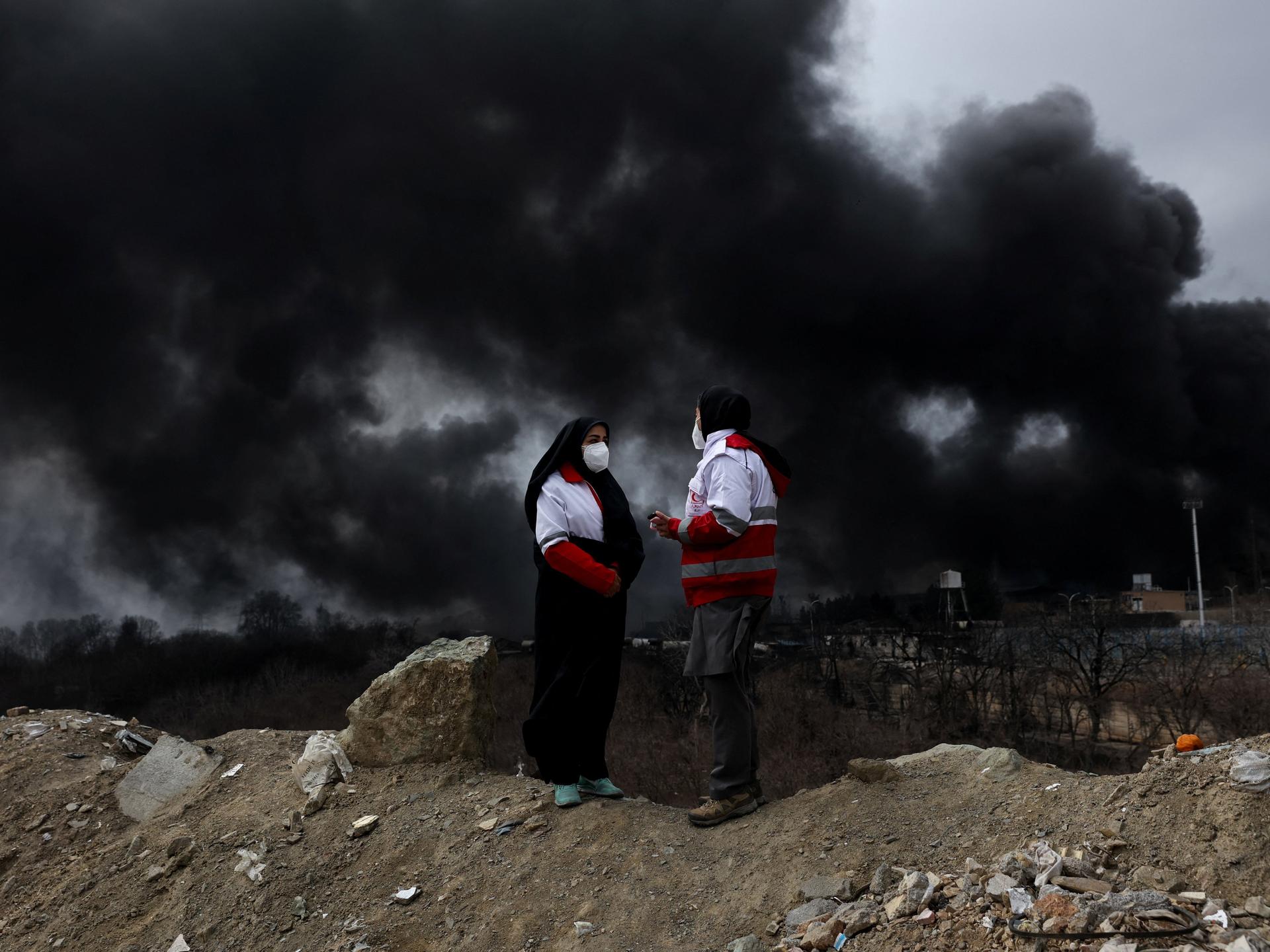 Members of the Red Crescent talk to each other as smoke rises after a reported strike on Shahran fuel tanks, amid the U.S.-Israeli conflict with Iran, in Tehran, Iran, March 8, 2026.