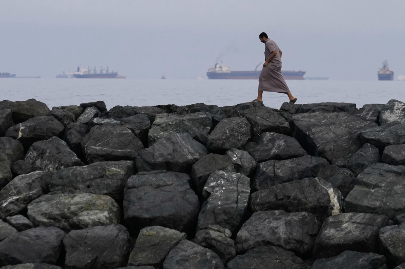 A man walks along the shore as oil tankers and cargo ships line up in the Strait of Hormuz, seen from Khor Fakkan, United Arab Emirates, Wednesday, March 11, 2026. Altaf Qadri/AP Photo