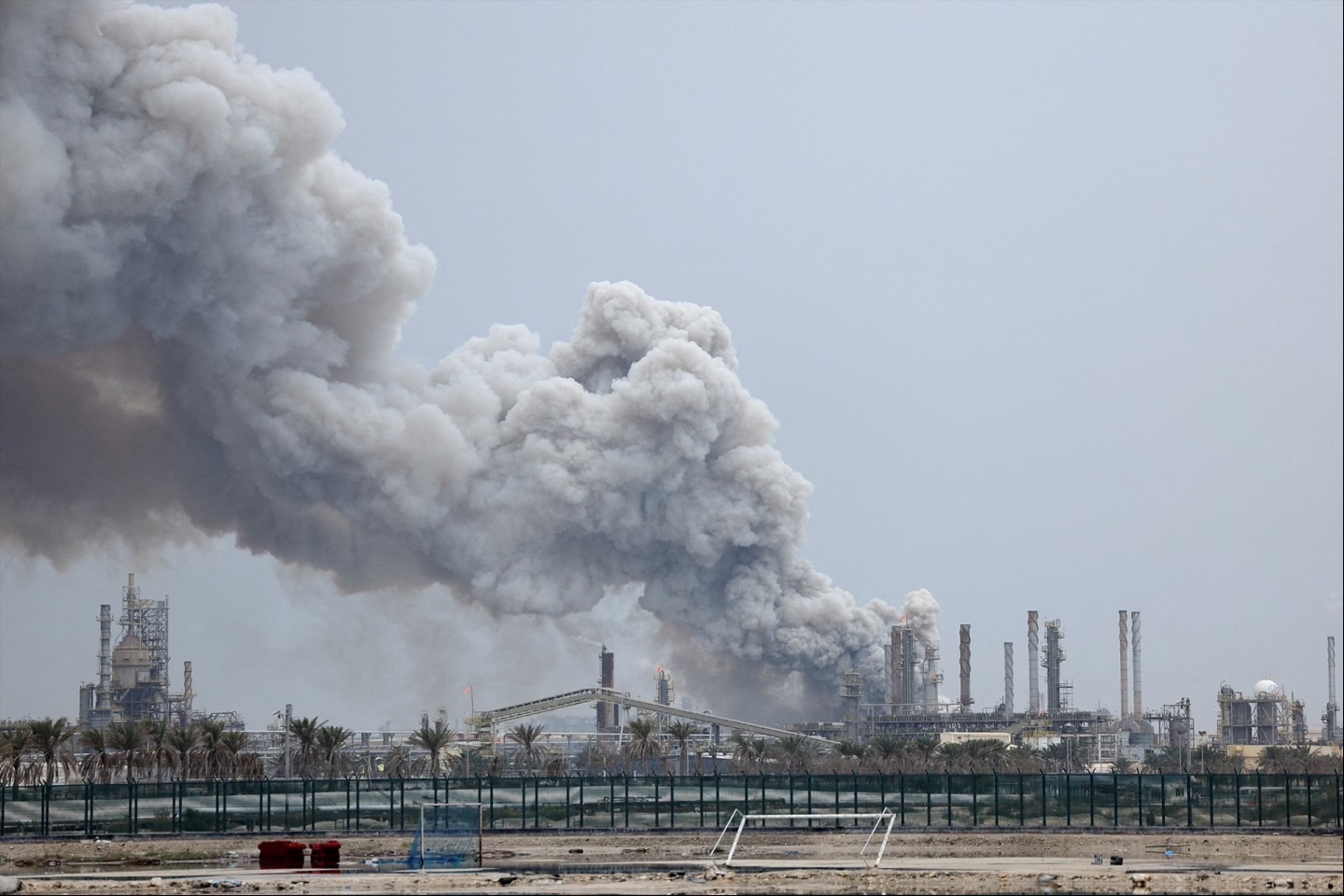 A person rides on a scooter as smoke rises in the Fujairah oil industry zone following a fire caused by debris after interception of a drone by air defenses, in Fujairah, United Arab Emirates, March 3, 2026.