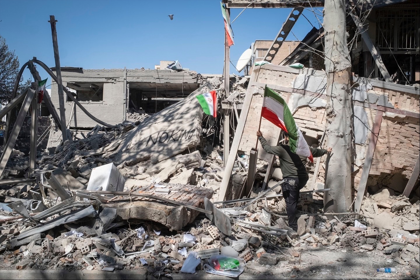 An unidentified man places a national flag on the ruins of the Sharif University of Technology’s data center, which was struck on April 6 during ongoing military operations in Tehran, Iran, on April 7, 2026. 