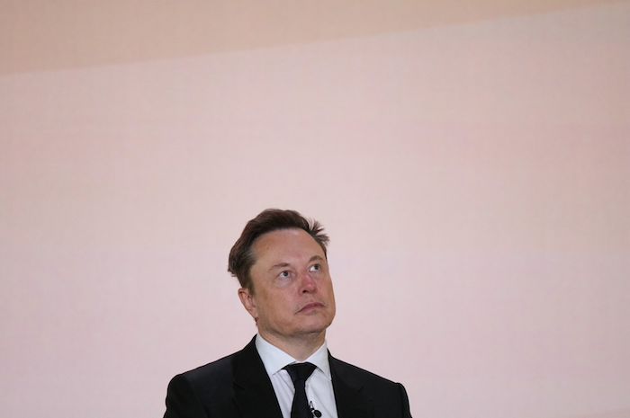 Elon Musk, shown from the chest up, stares off into the distance with a bored expression.
