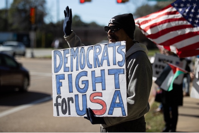 A protester holds a sign at a demonstration outside Texas Senator John Cornyn's office in Houston on December 30, 2025. Reginald Mathalone/NurPhoto/AP