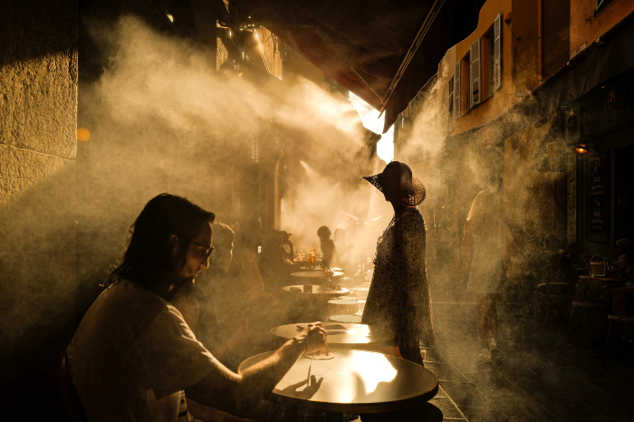 Several people shelter from the sun under an awning along a line of outdoor stores.