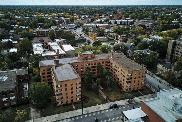 A large, U-shaped apartment building made of tan brick in an urban setting as seen from above.