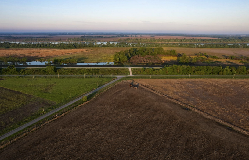An aerial view of flat farmland in the foreground and rivers in the background, under a blue southern Illinois sky. 