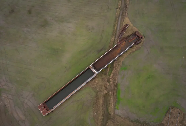 An aerial view of a large barge stranded on farmland. 