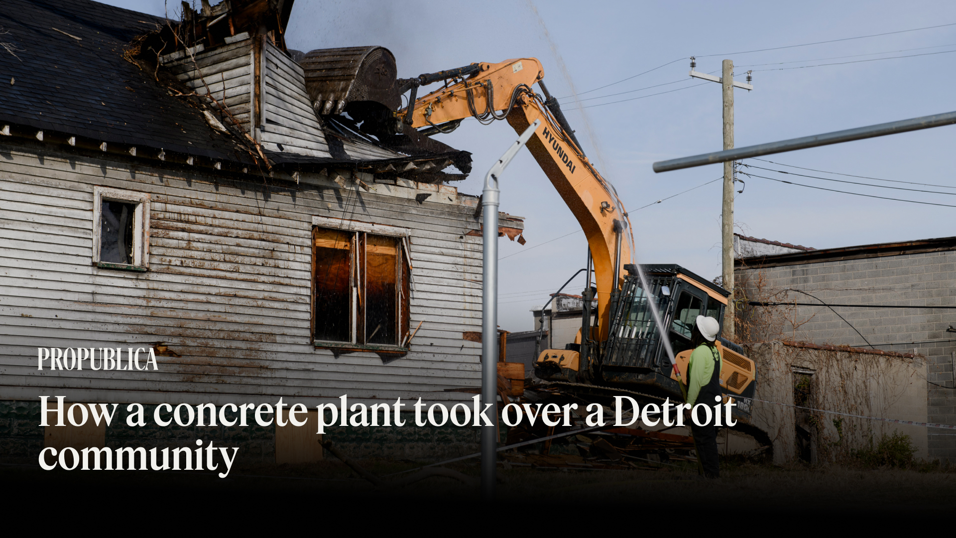 A large machine dismantles the roof of a house as a worker looks on in the foreground.